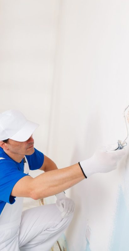 side view of  painter in white dungarees, cap and gloves painting a wall with paint roller and wooden vintage ladder, with copy space